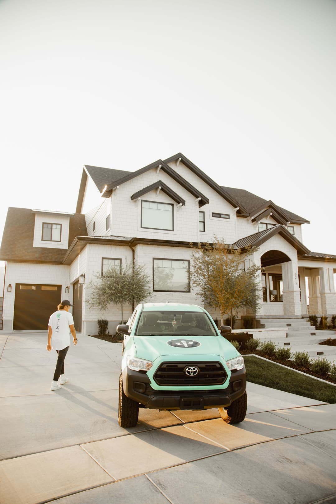 Person walking towards a modern home with a mint green Toyota truck parked in the driveway.