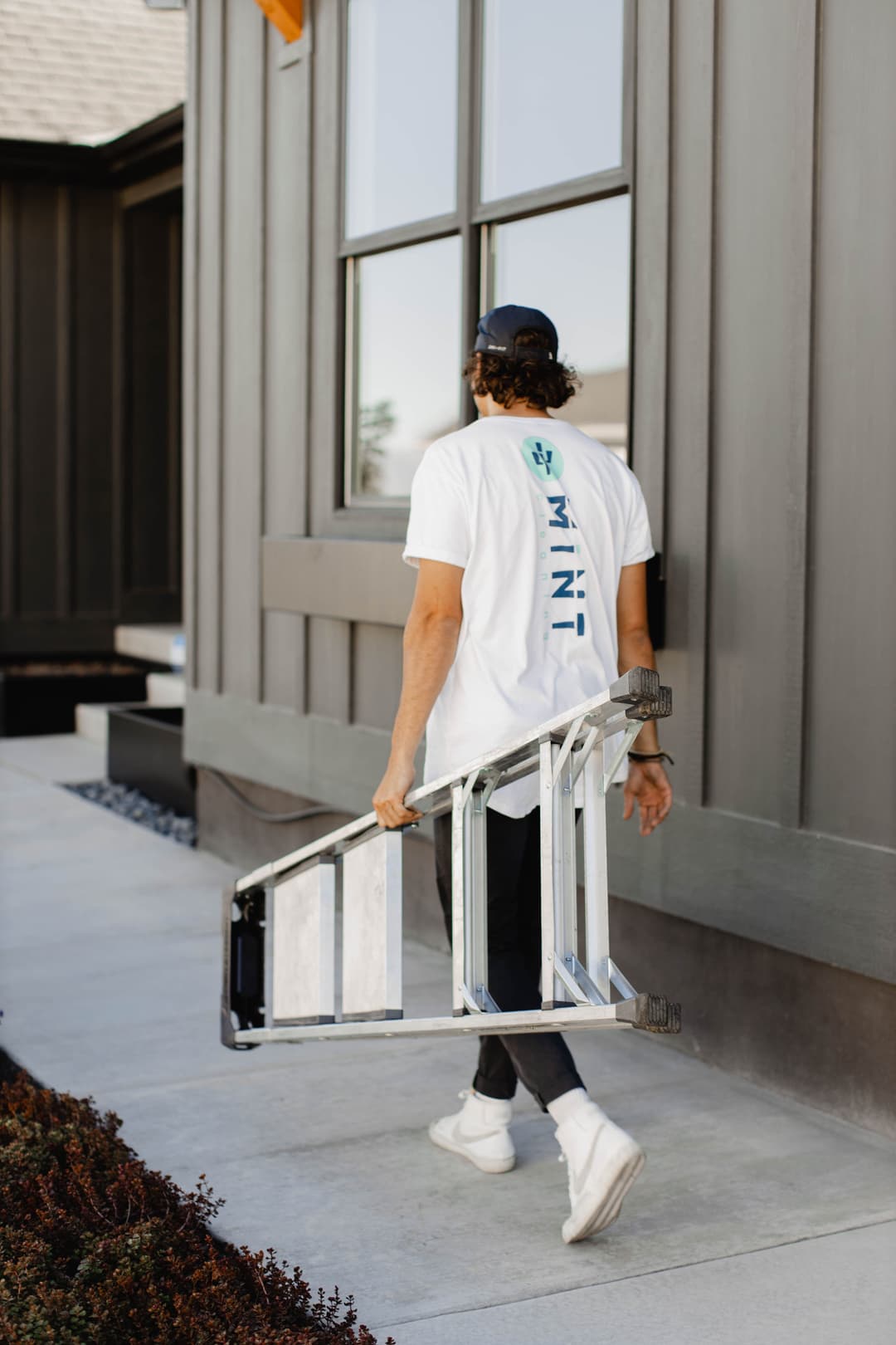 Person carrying a folding ladder outside a modern home, showcasing home improvement activities.