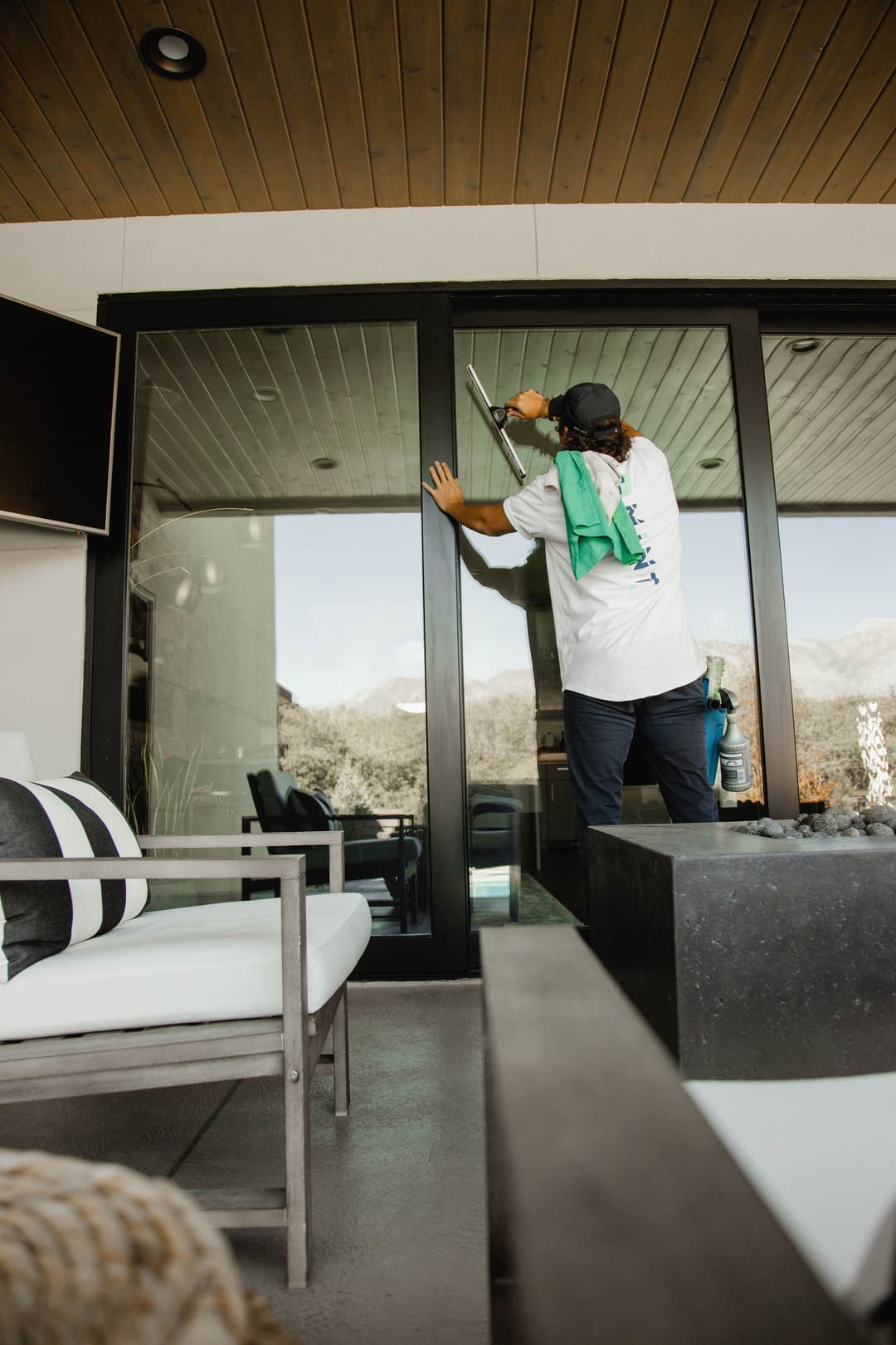 Person cleaning glass doors with a squeegee, surrounded by modern outdoor furniture.