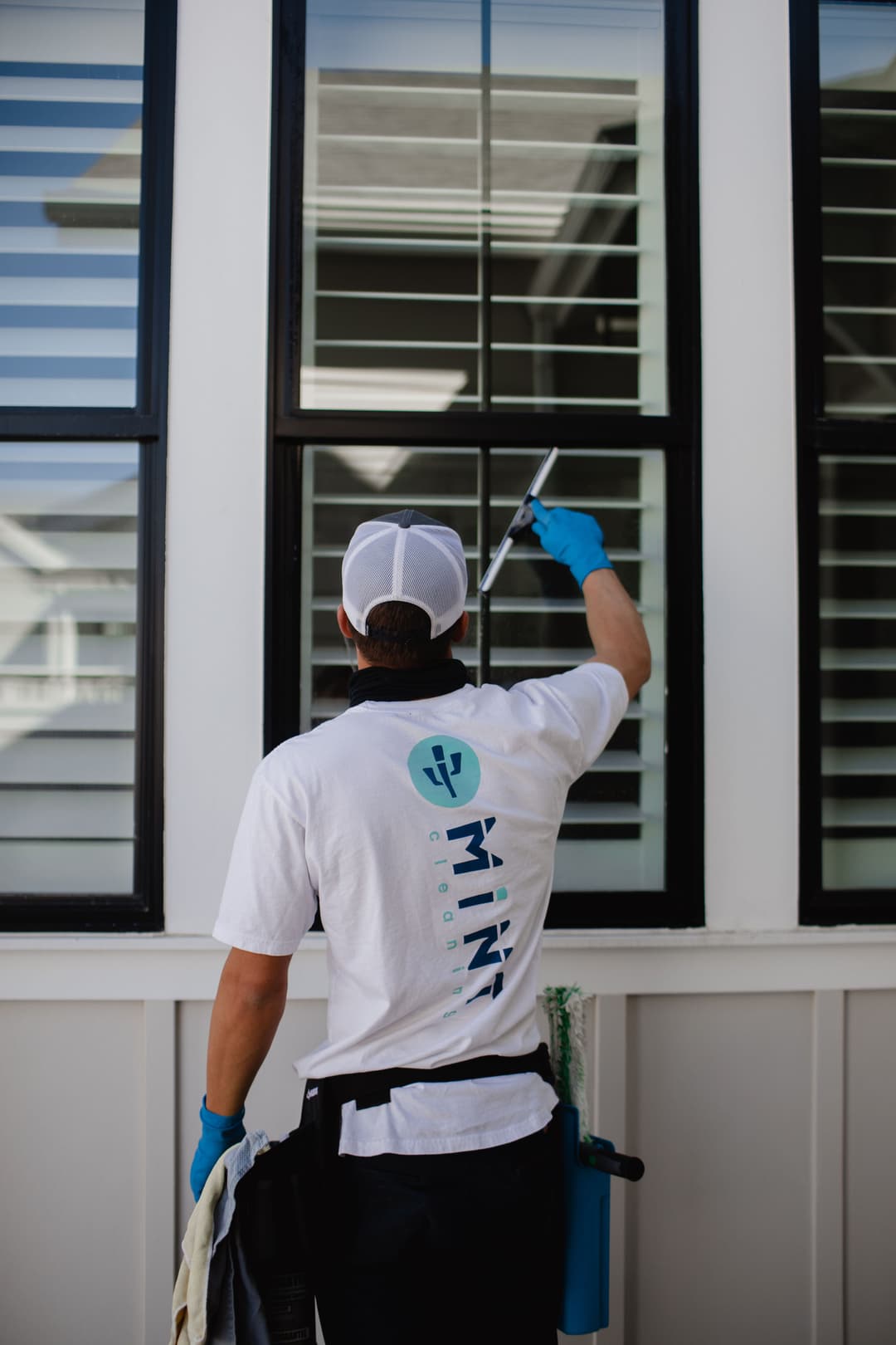 Window cleaner in blue gloves and uniform using a squeegee on a home's glass windows.