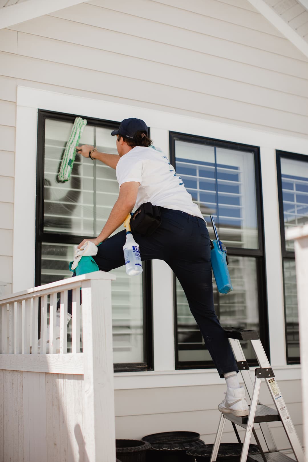 Man cleaning a window on a ladder; outdoor home maintenance and window washing service.