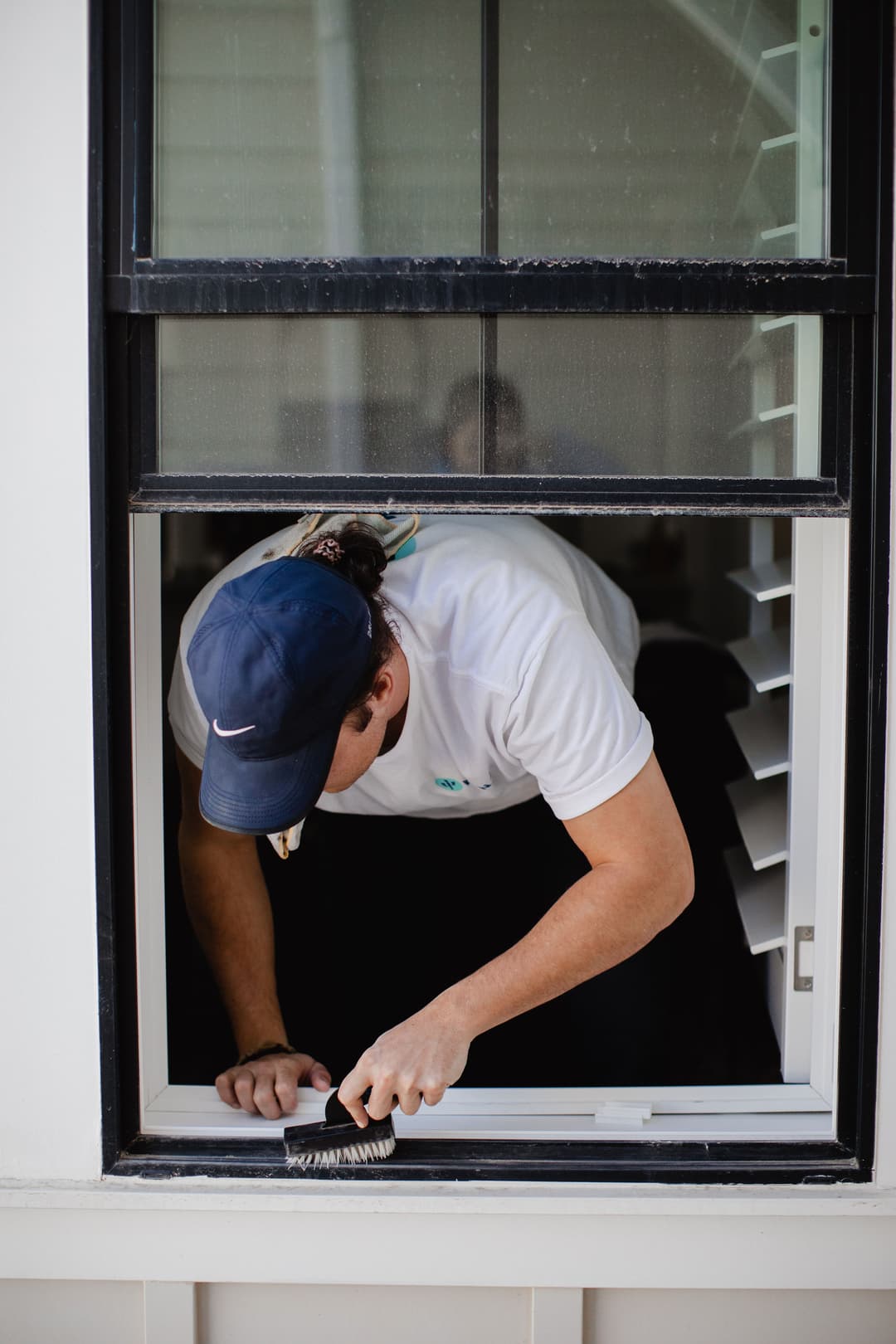 Maintenance worker cleaning window frame from the outside with a brush.