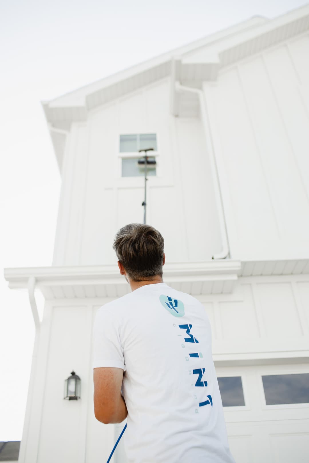 Man using a pole to clean a high window on a modern white house.
