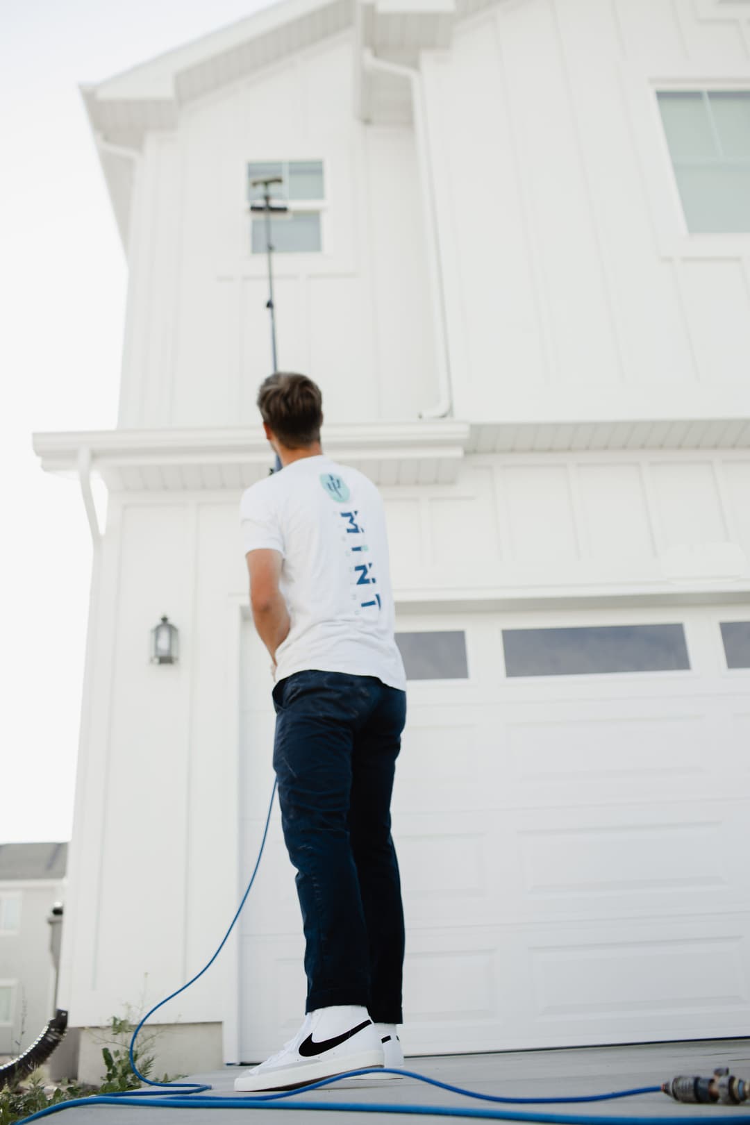 Man using a pole to clean a high window on a modern white house exterior.