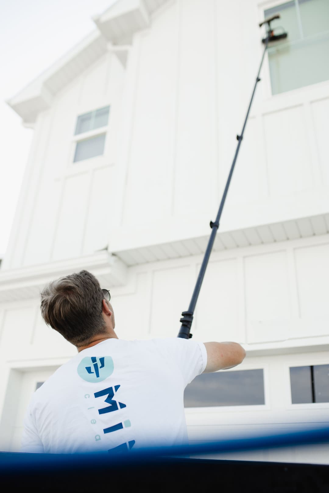 Man cleaning a high window with a long extension pole on a modern white house.