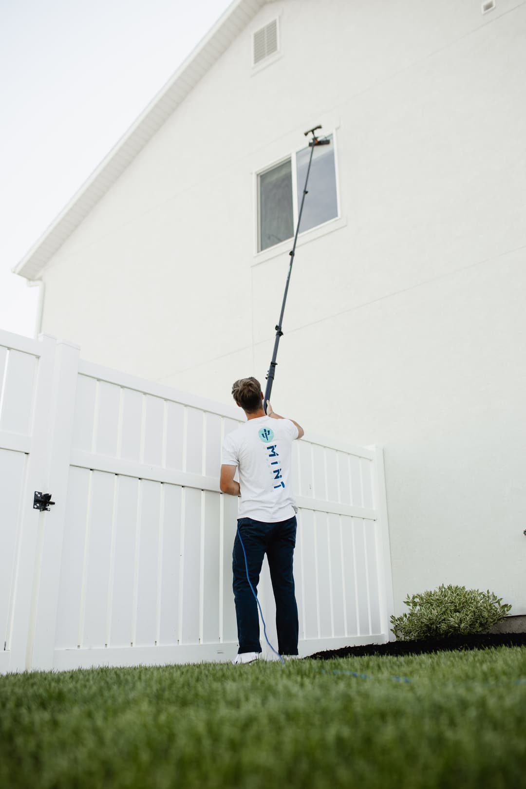 Person using a long pole to clean a window on a two-story white house.