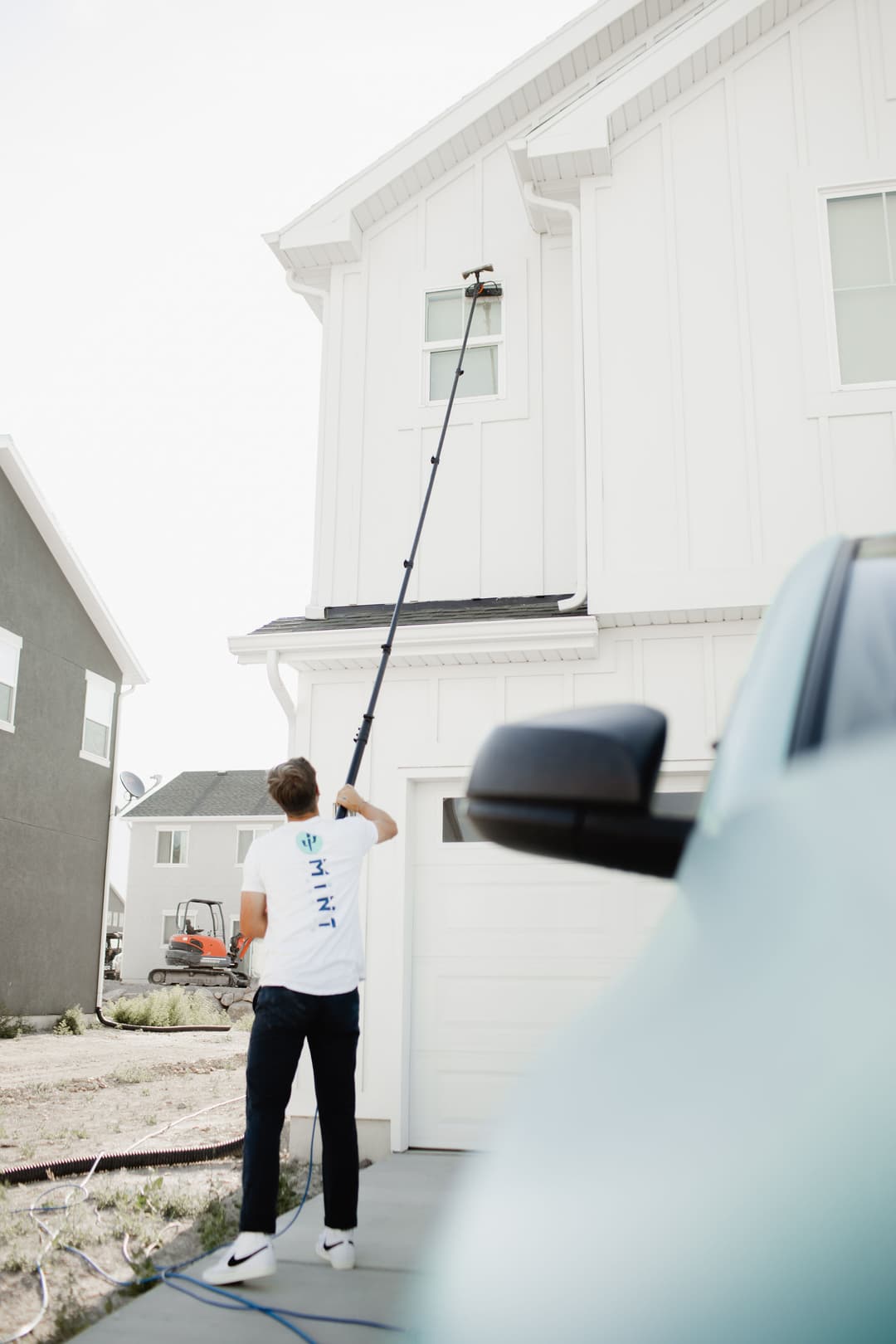 Person using a pole to clean windows on a modern house exterior. Bright sunlight, residential setting.