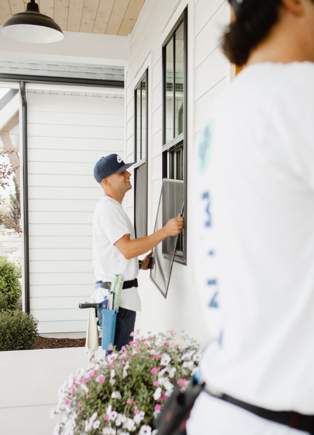 Home window installation with professionals adjusting a screen on a white house exterior.