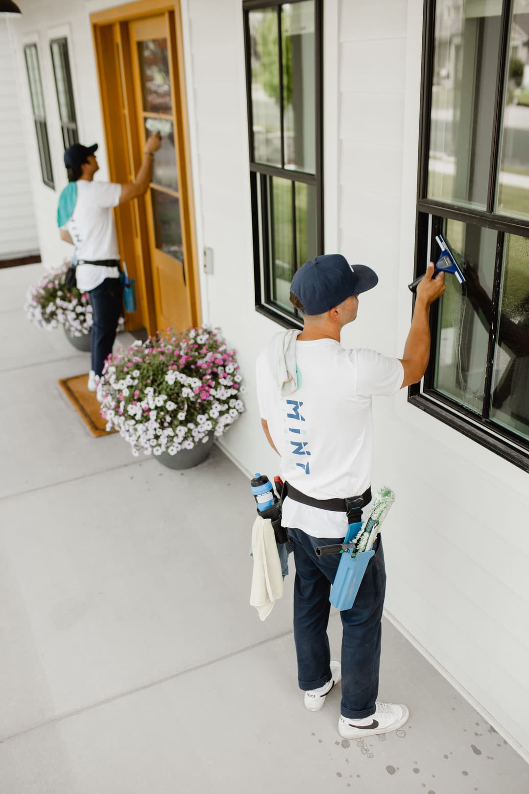 Two workers cleaning windows on a modern home, showcasing a professional cleaning service.