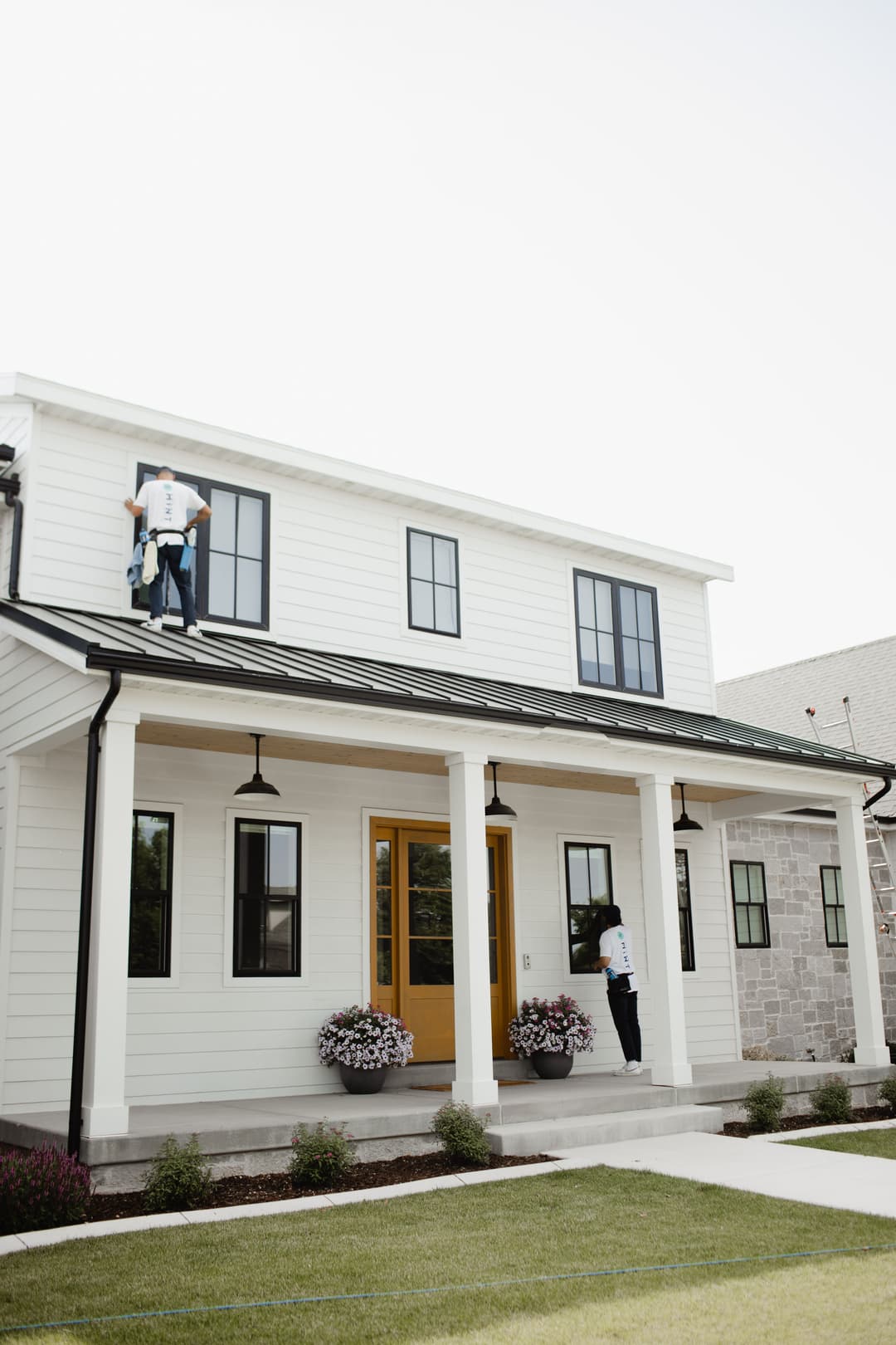 Workers cleaning windows on a modern two-story house with a white exterior and yellow door.