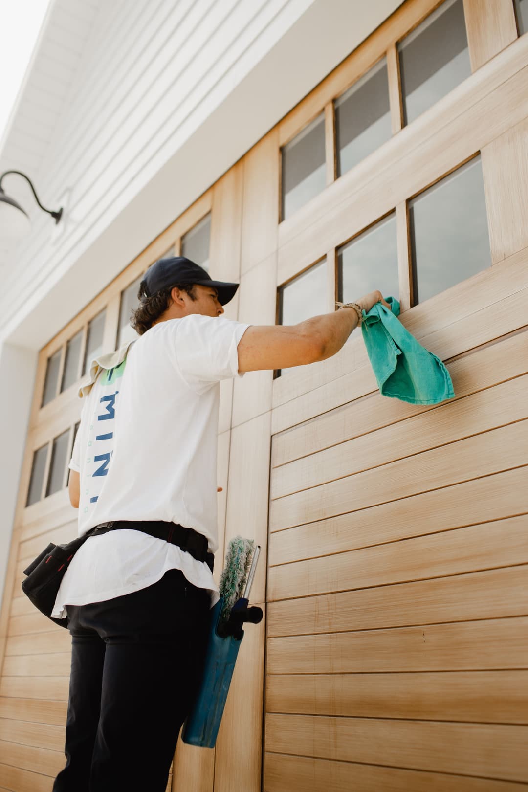 Person cleaning wooden garage doors with a cloth and cleaning tools, enhancing home aesthetics.