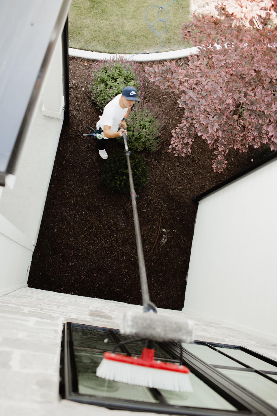 Man cleaning a high window with a squeegee and pole on a residential property.