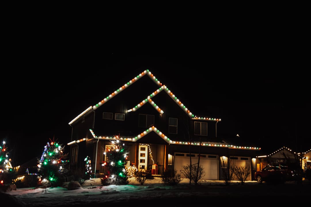 Festively decorated house with Christmas lights and trees during nighttime winter season.