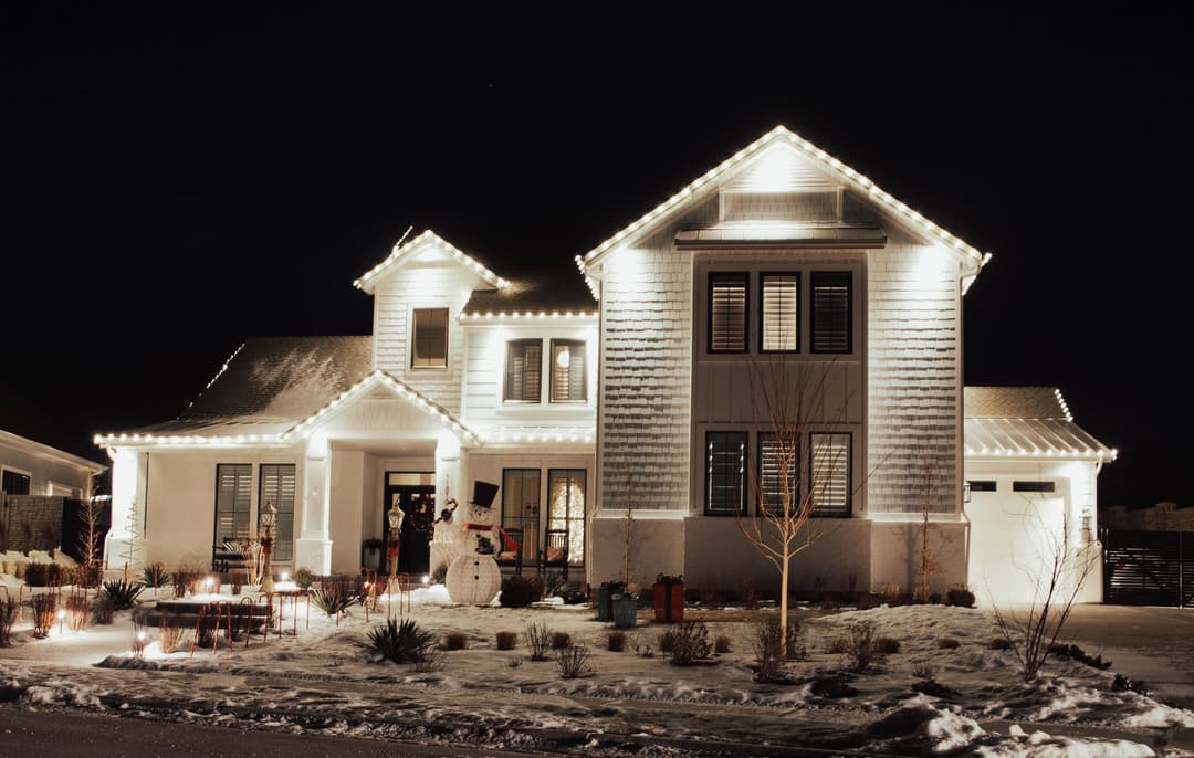Festively lit winter house with snowman and holiday decorations at night.