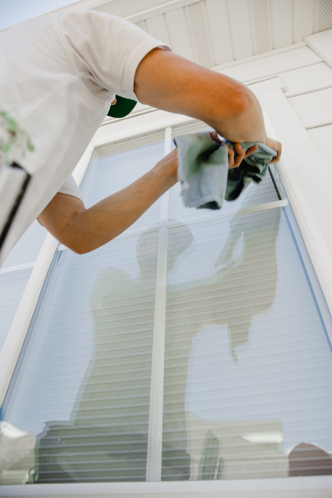 Person cleaning a window with a cloth, showcasing a reflection on the glass surface.