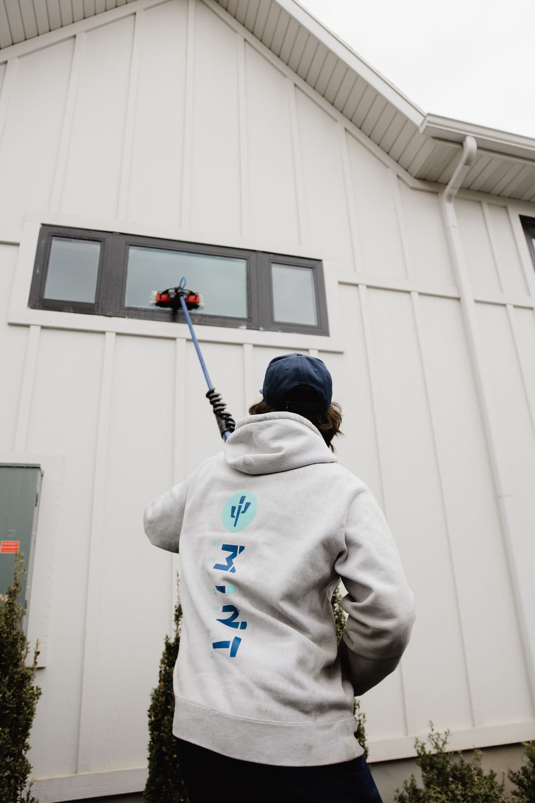 Person in a gray hoodie cleaning a high window with a long squeegee on a building exterior.