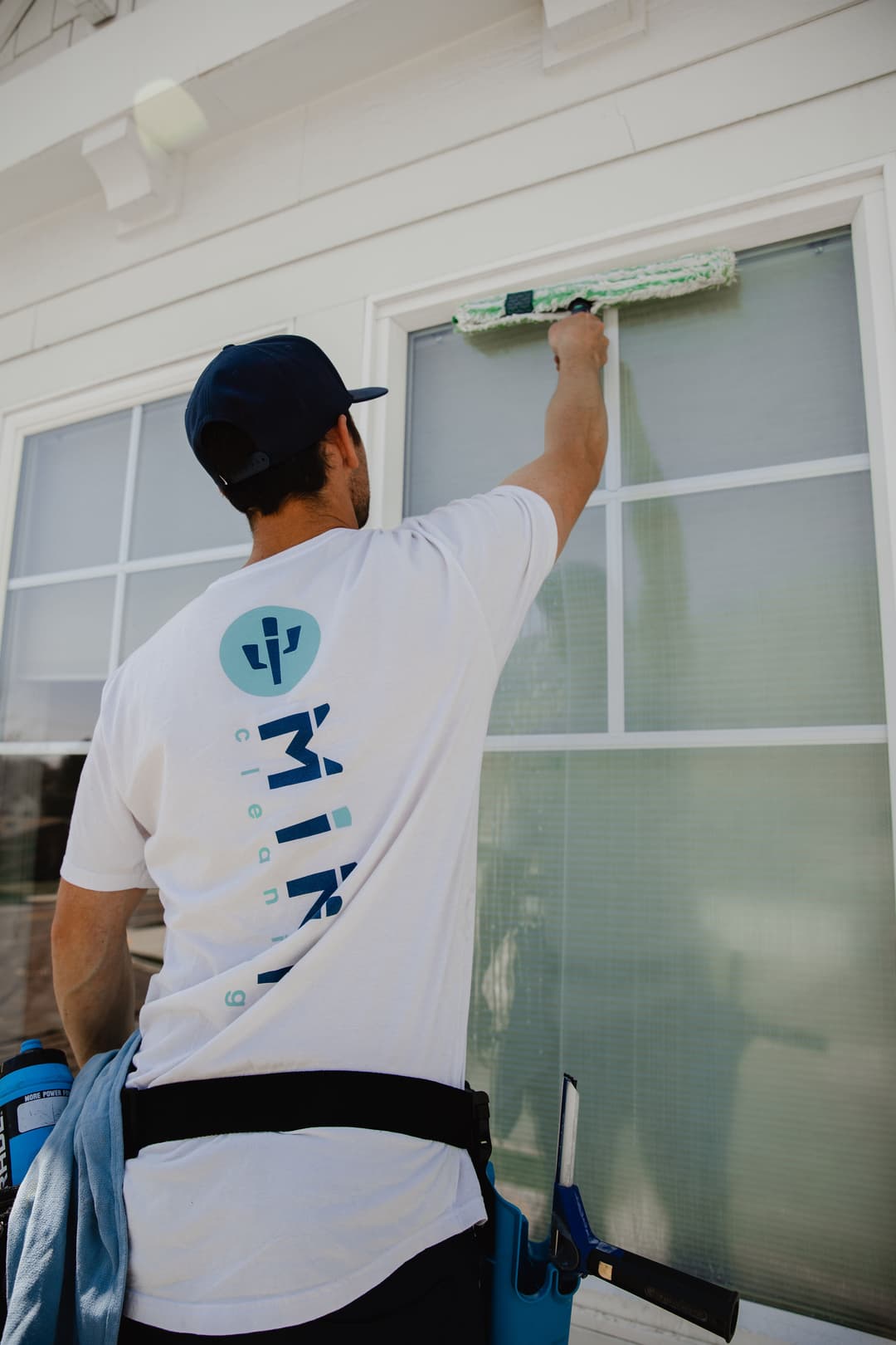 Person cleaning a window with a roller, wearing a branded shirt for a cleaning company.