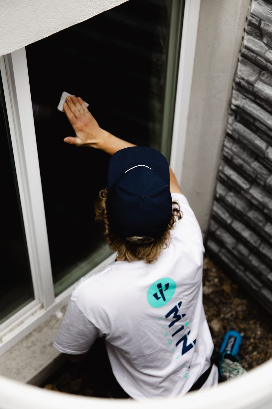 Professional window cleaner wearing a branded shirt and cap, cleaning glass in a modern setting.