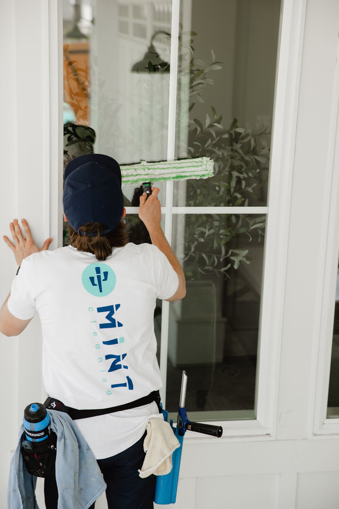 Window cleaner from Mint Cleaning using a squeegee on a glass window with plants in the background.