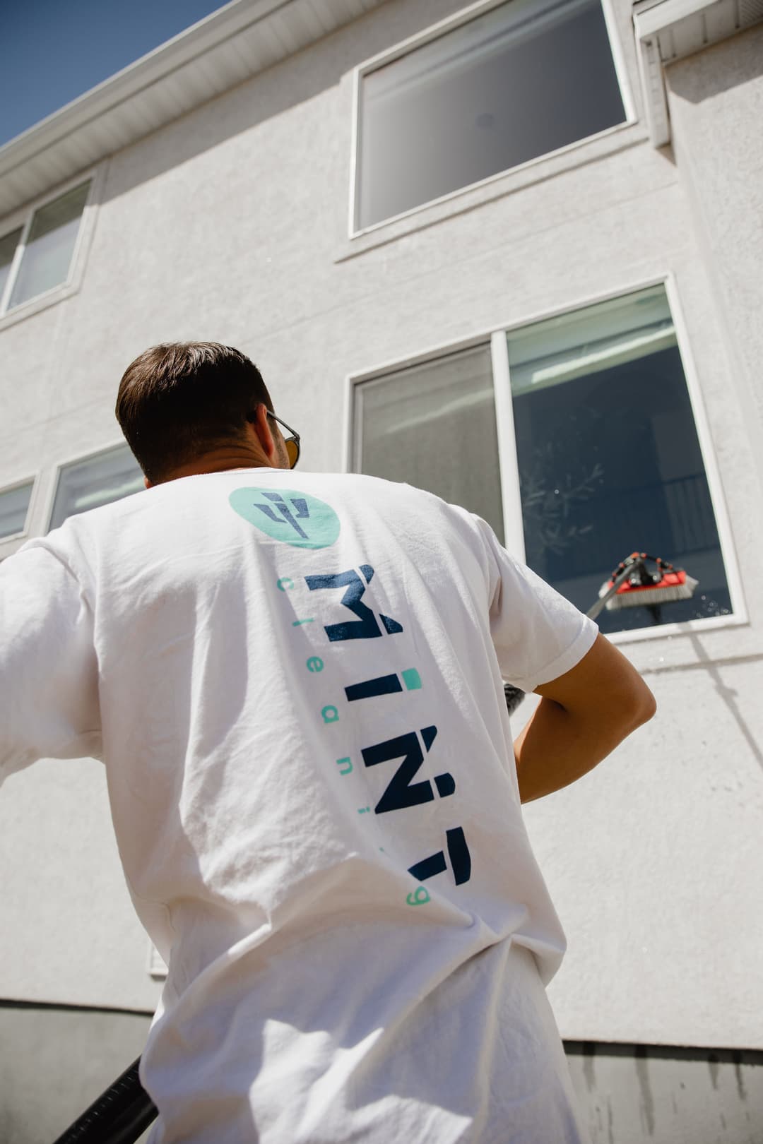 Man in a Mint Cleaning shirt washing windows of a residential building on a sunny day.