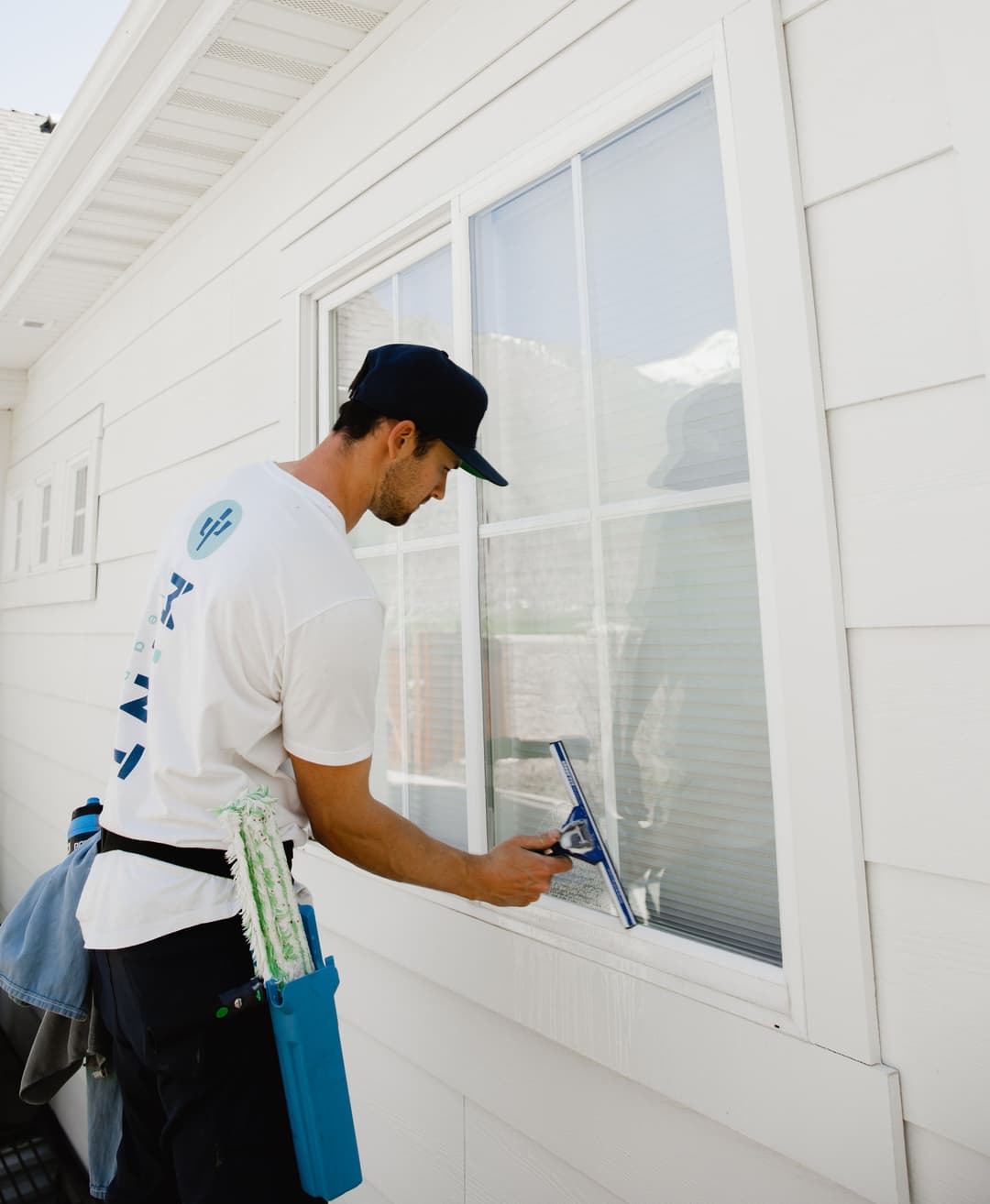 Man cleaning a window with a squeegee, wearing a white T-shirt and a cap.