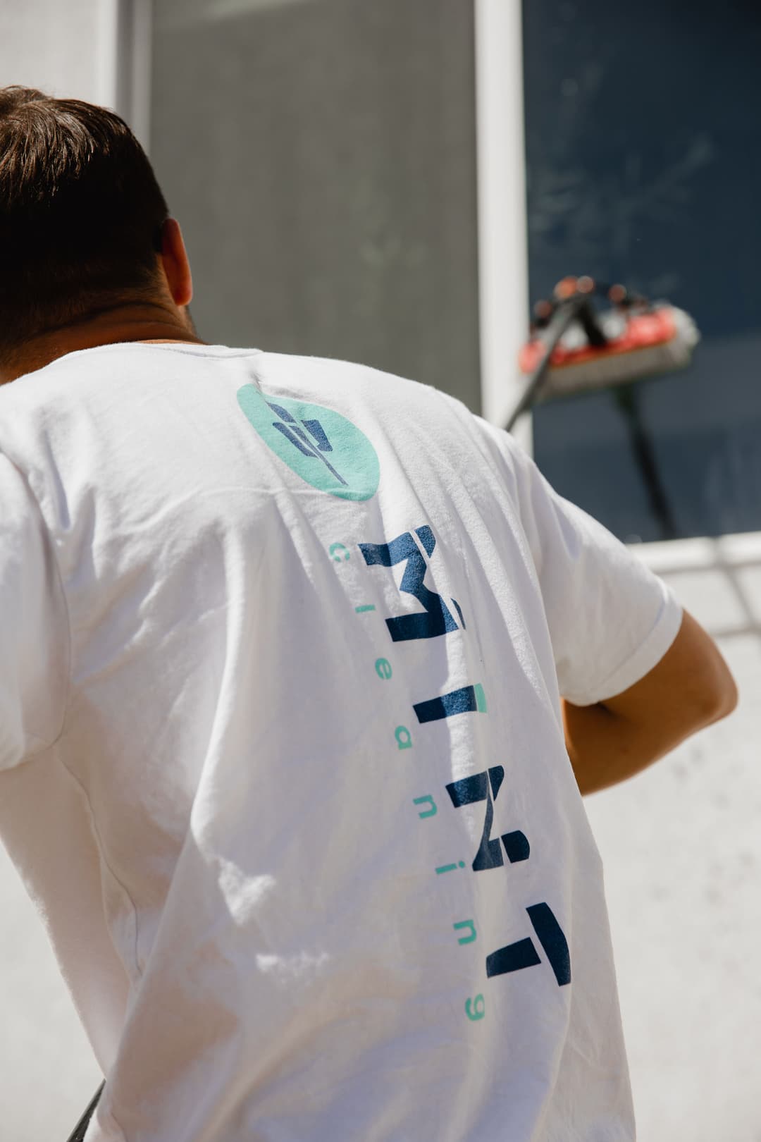 Man in white t-shirt cleaning a window, showcasing the logo of the cleaning company.