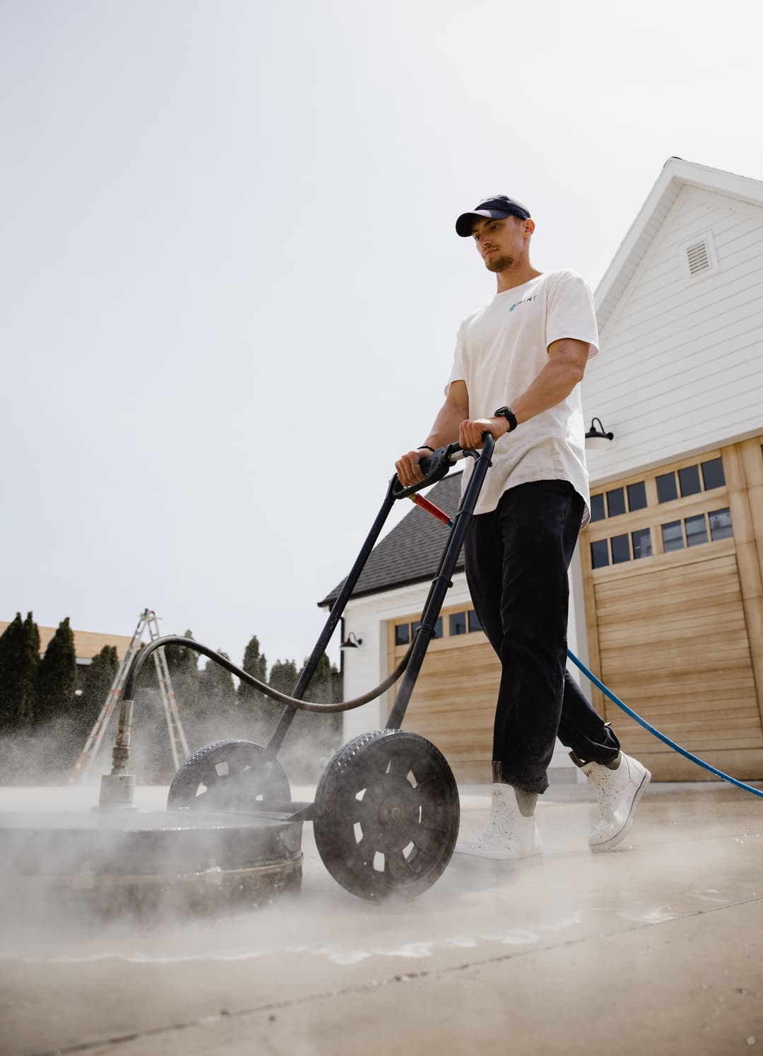 Man using a pressure washer on a driveway, creating mist and cleaning surface.