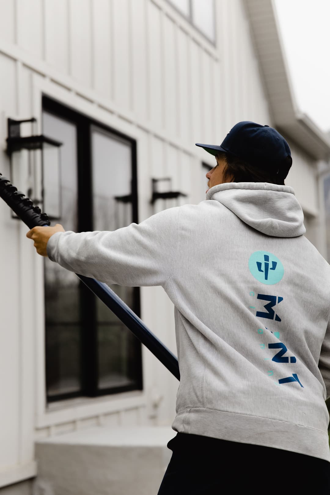 Person in a gray hoodie with mint blue design, holding a blue pole near a modern building.
