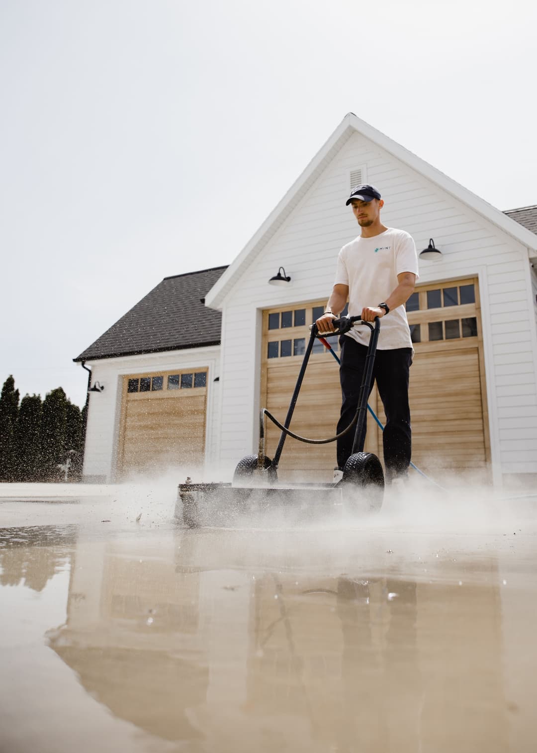 Person using a surface cleaner on a wet driveway in front of a modern home.