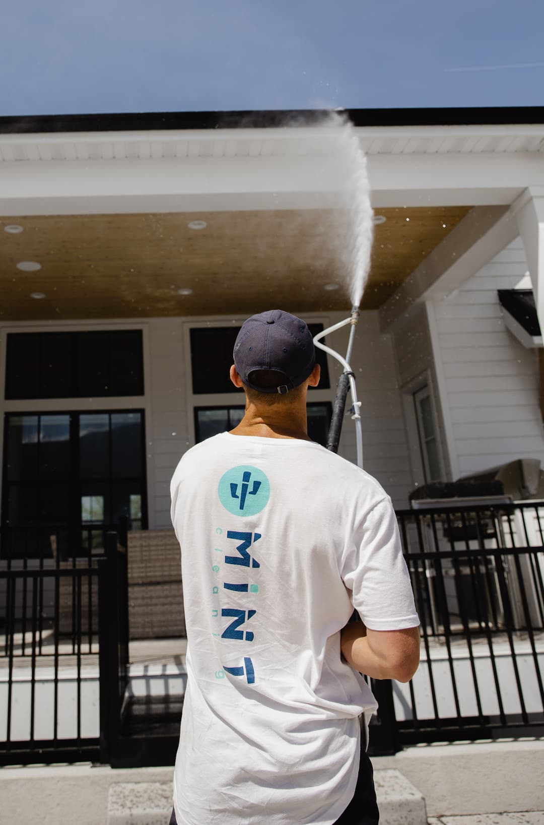 Man pressure washing a house exterior wearing a branded shirt with "MIND" logo.
