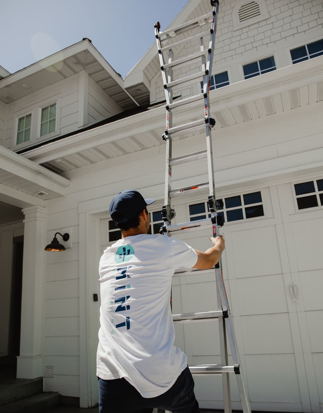 Person climbing a ladder to work on a home exterior under clear blue skies.