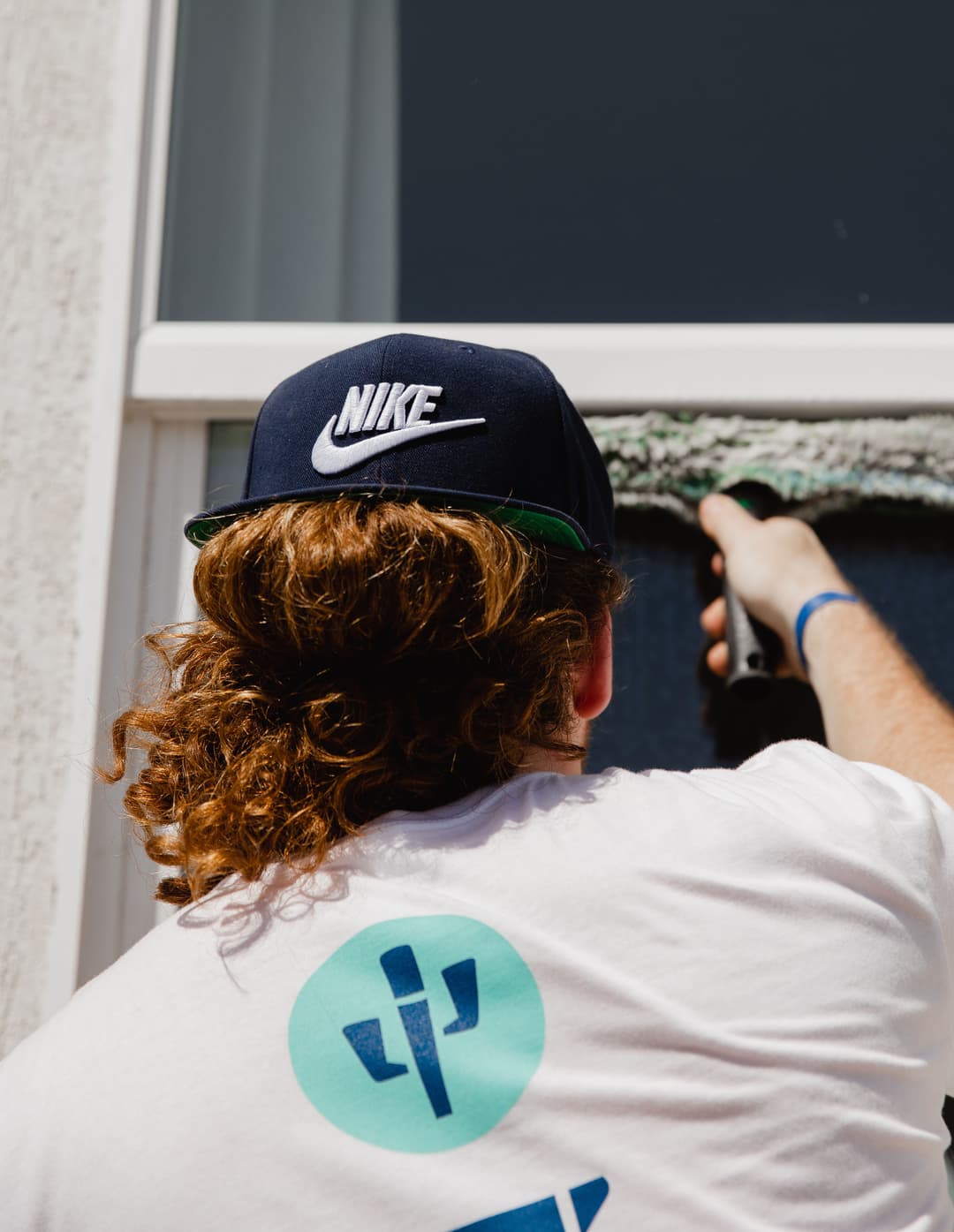 Person cleaning a window, wearing a Nike hat and a white shirt with a cactus design.