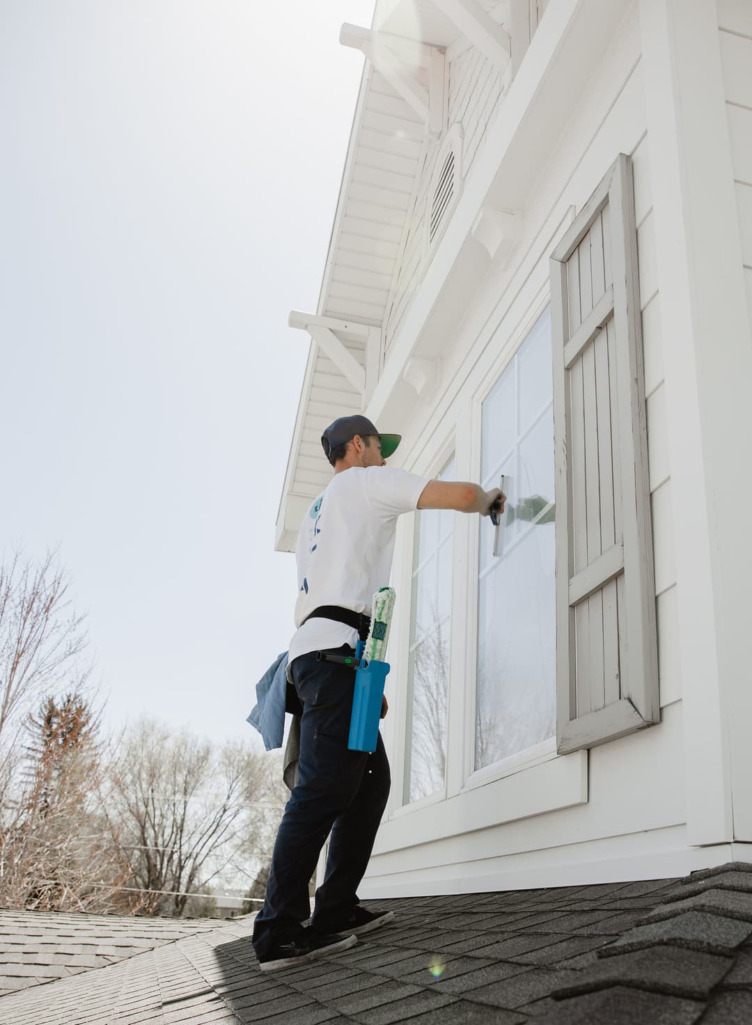 Person cleaning a window on a house, using a squeegee and wearing casual work attire.