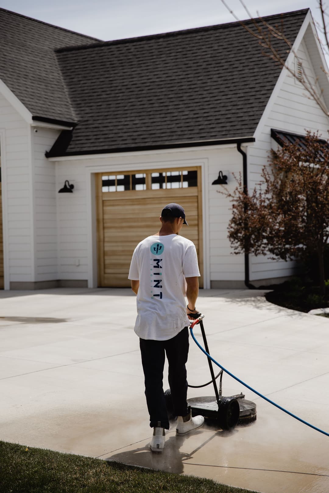 Man using a pressure washer on a driveway near a modern home with a white exterior.
