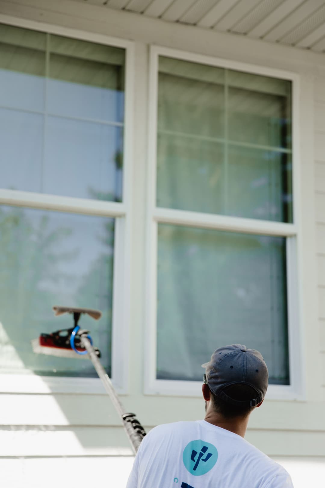 Man using a extendable squeegee to clean large windows on a house exterior.