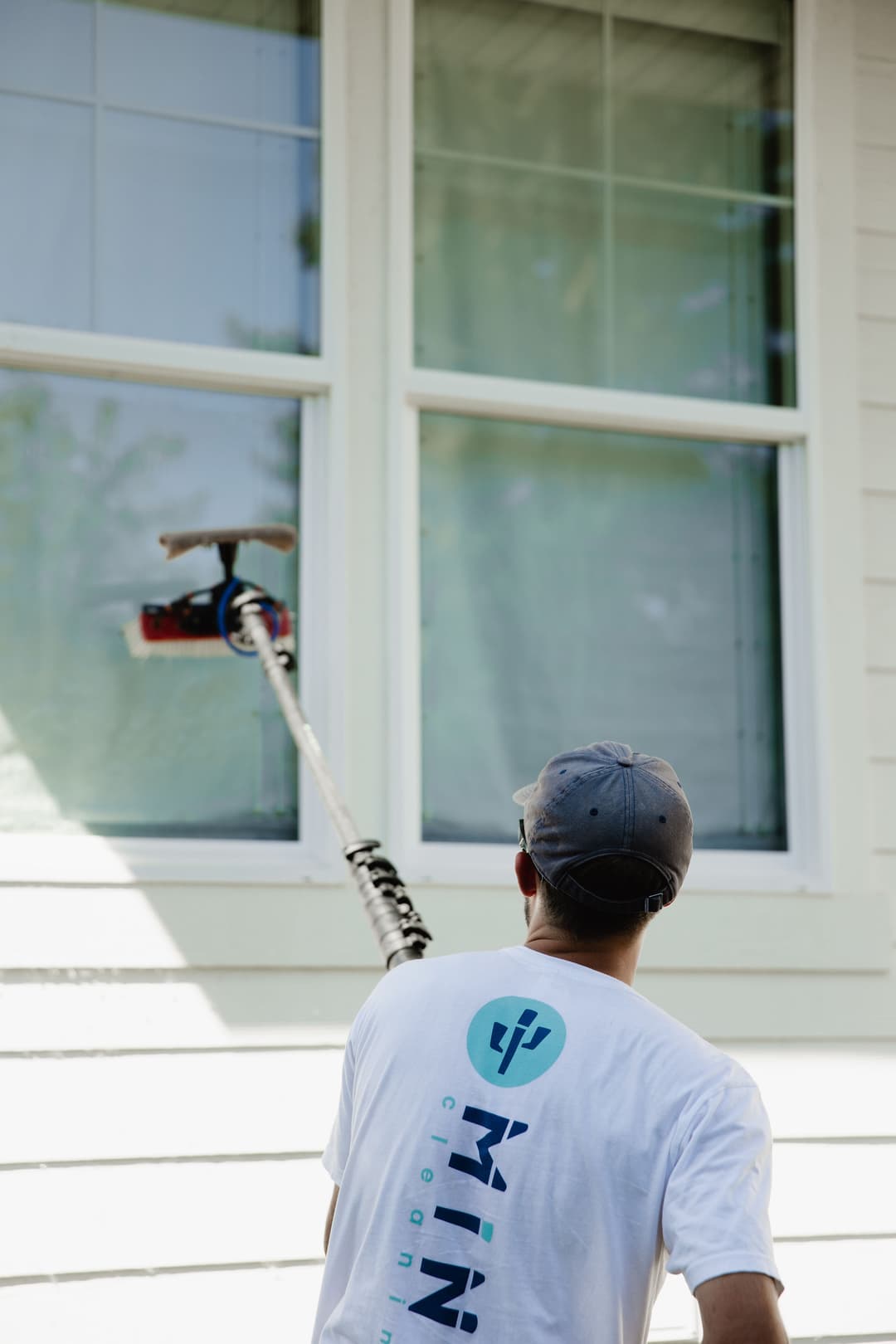 Man cleaning windows with extendable pole, wearing a branded shirt for a cleaning service.
