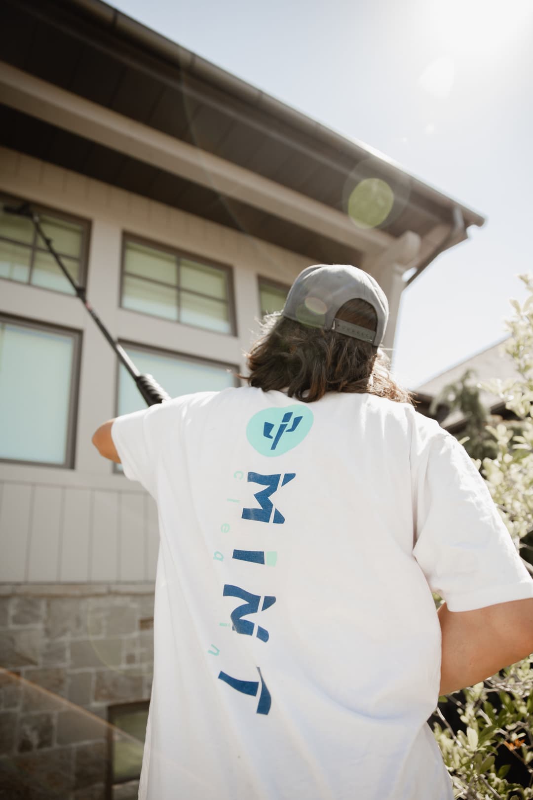 Person wearing a white shirt with a graphic design and a hat, cleaning a building exterior.