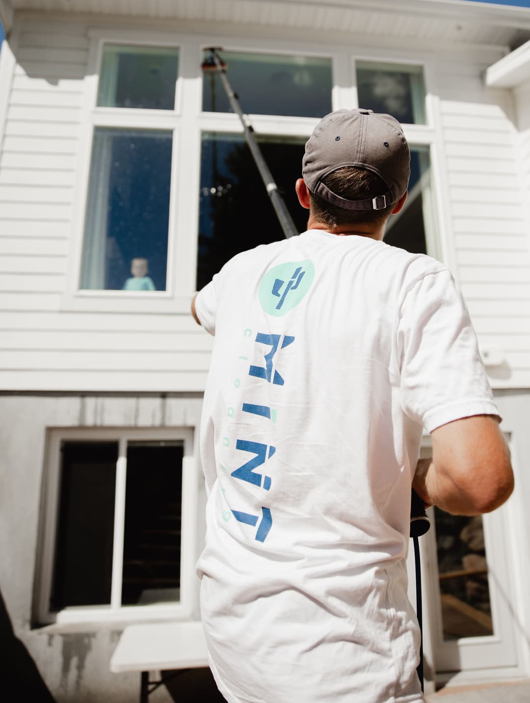 Man cleaning large window with professional equipment, wearing a branded shirt.