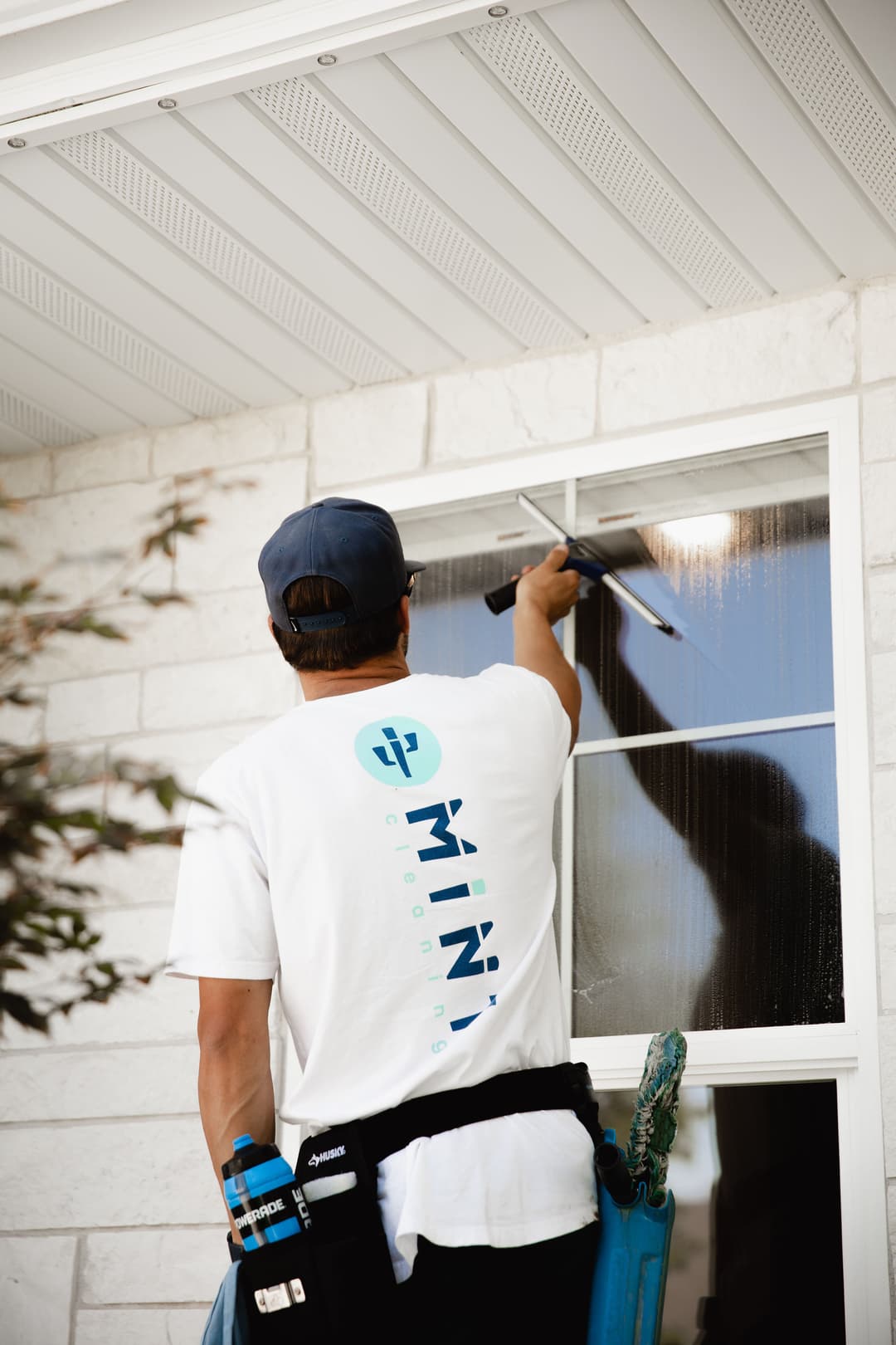 Window cleaner in a white shirt using a squeegee on a residential window.
