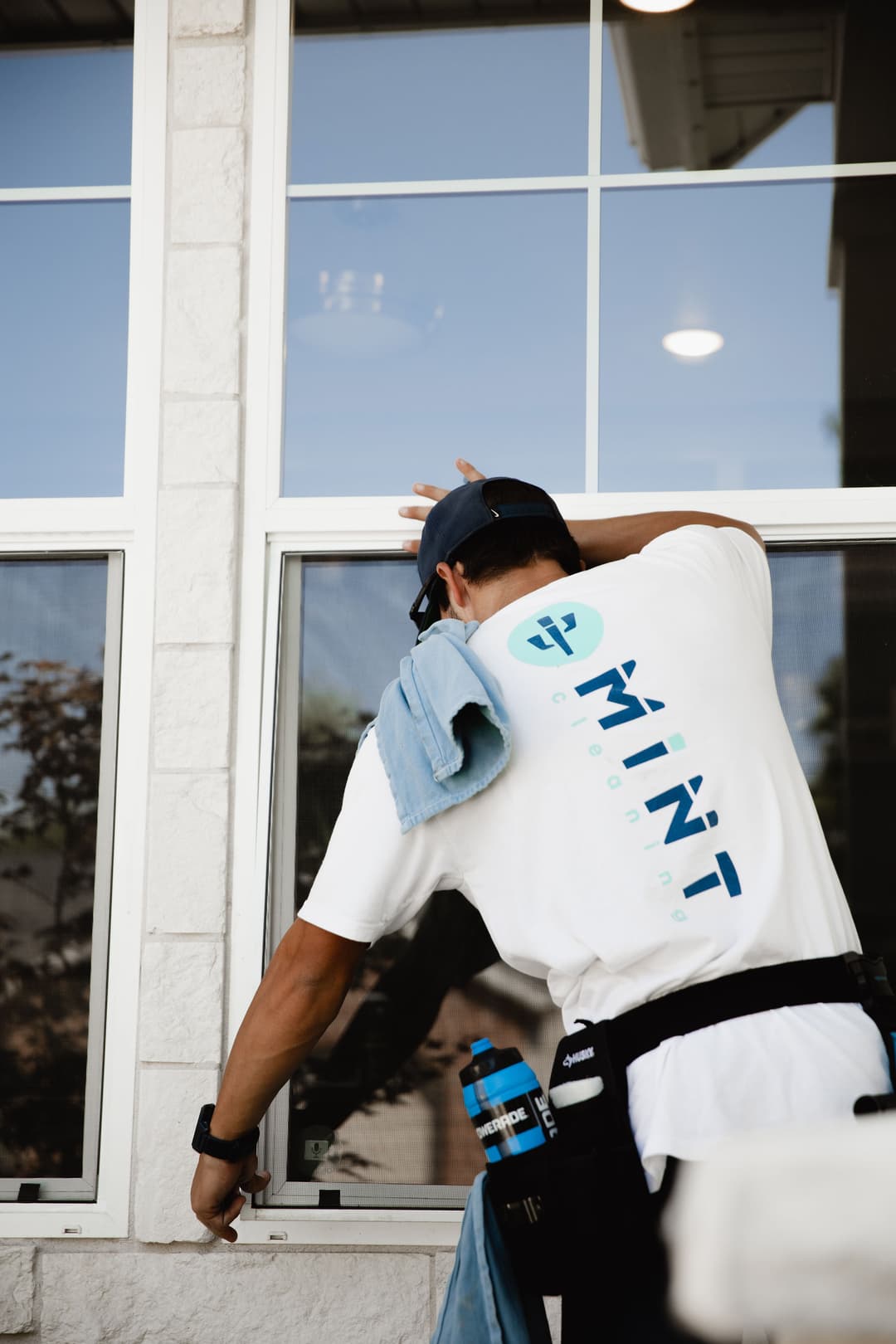 Man cleaning a window with a towel, wearing a branded Mint Cleaning shirt.