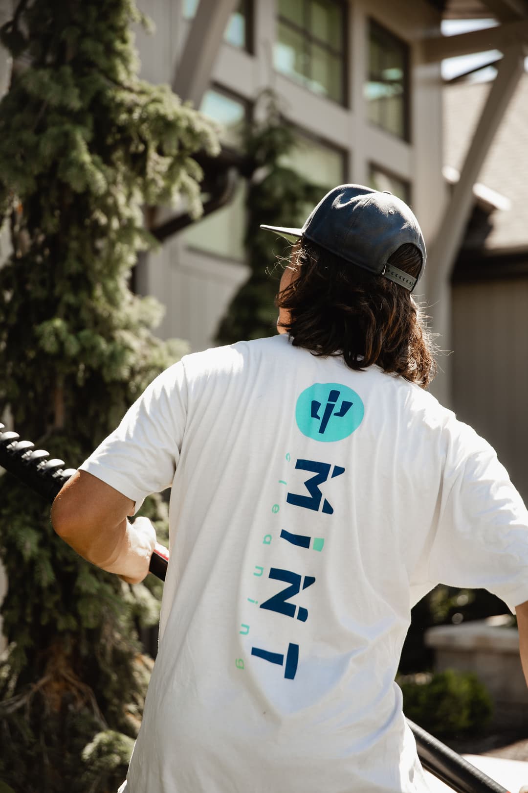 Person wearing a white t-shirt with "MINI" logo, holding a rope outdoors near a building.