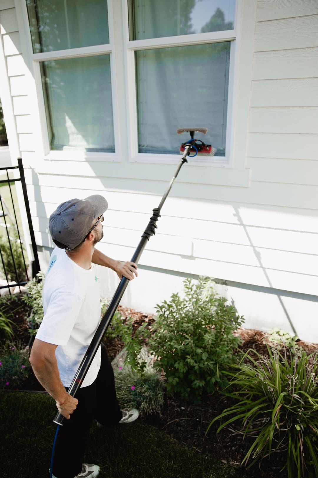 Man using a long pole to clean a window on a house exterior.