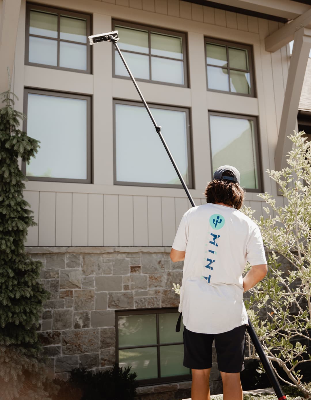 Person using a long pole to clean windows of a modern house with stone exterior.