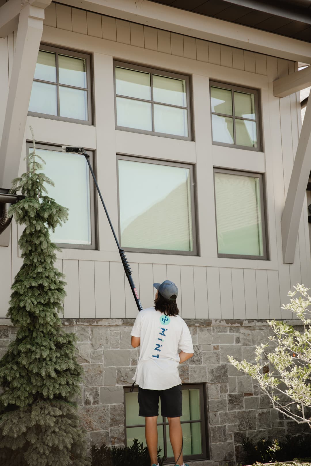 Man using a long pole to clean windows on a modern home exterior.