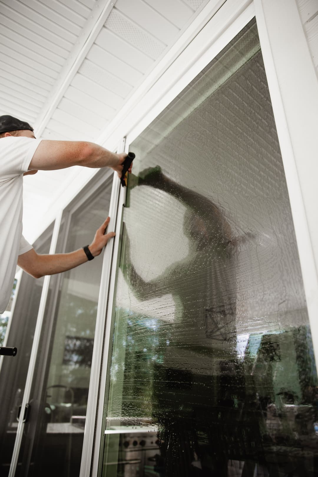 Person cleaning a large glass window using a squeegee, with a clear reflection visible.