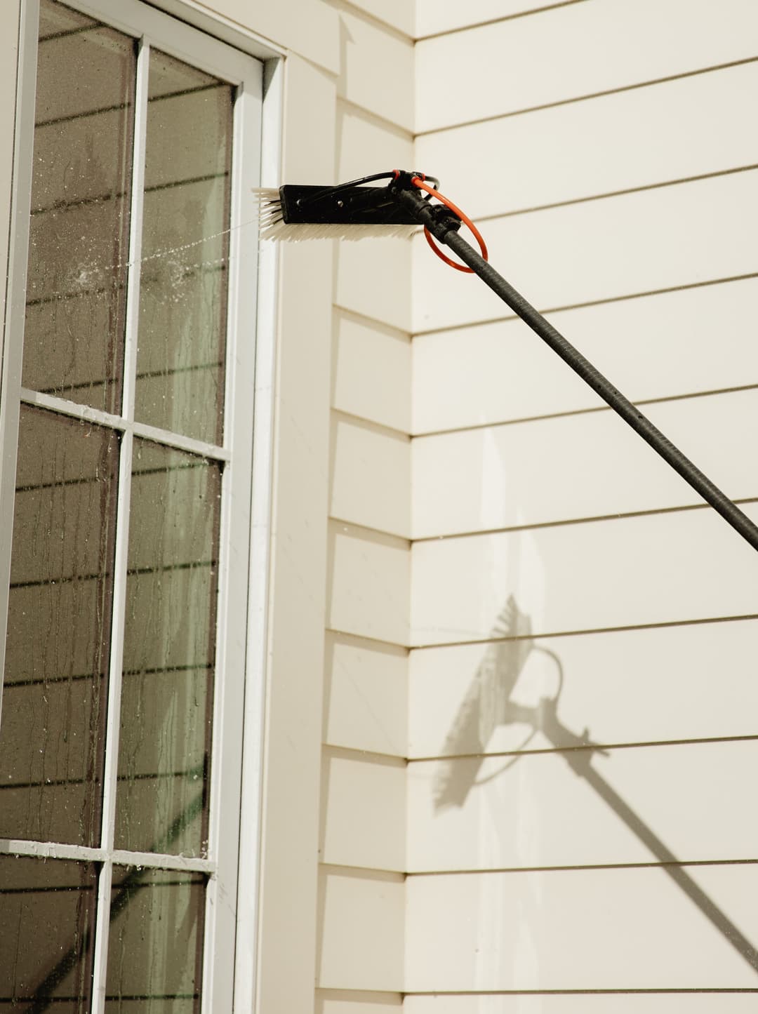 Long reach window cleaning tool in use on a glass window with a light-colored exterior wall.