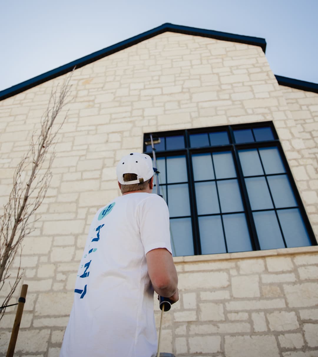 Person painting a tall building's exterior with a roller, blue sky above.