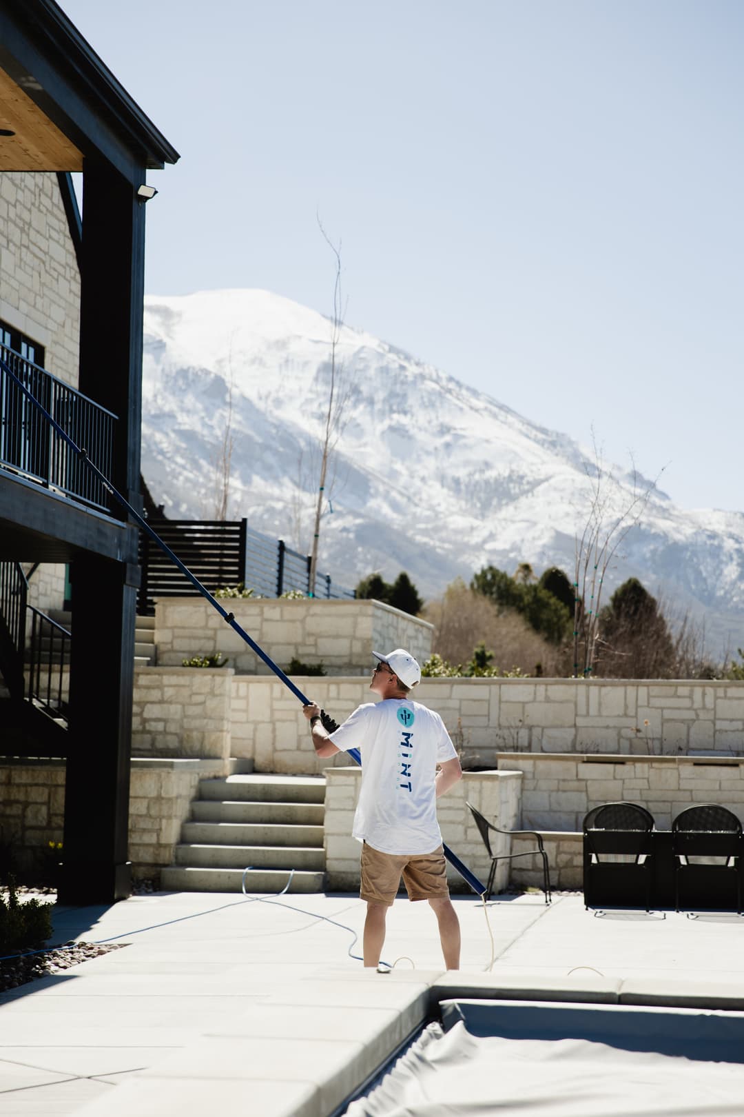 Man cleaning a poolside area with a mountain backdrop on a sunny day.
