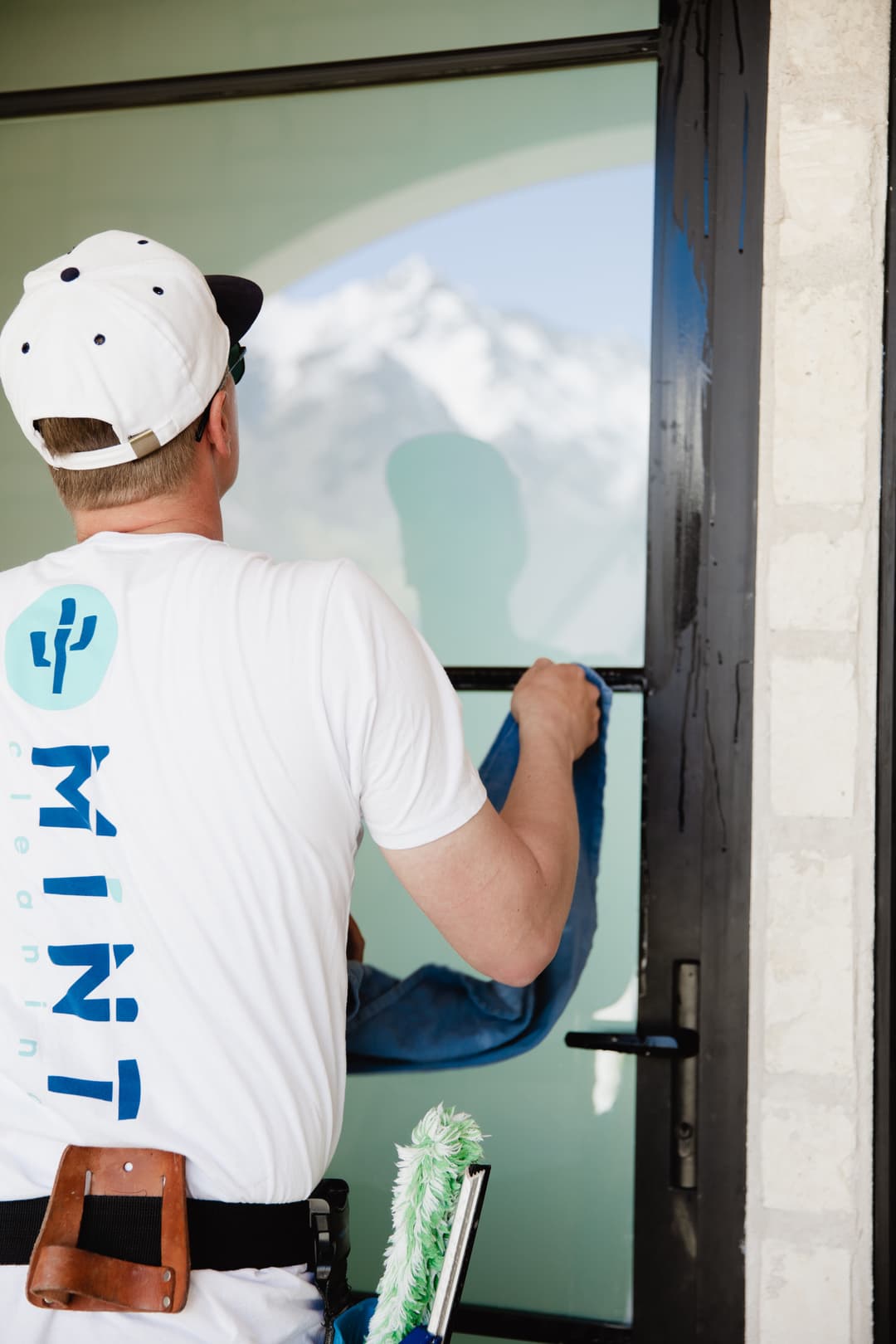 Window cleaning professional using a cloth on glass with mountains in the background.