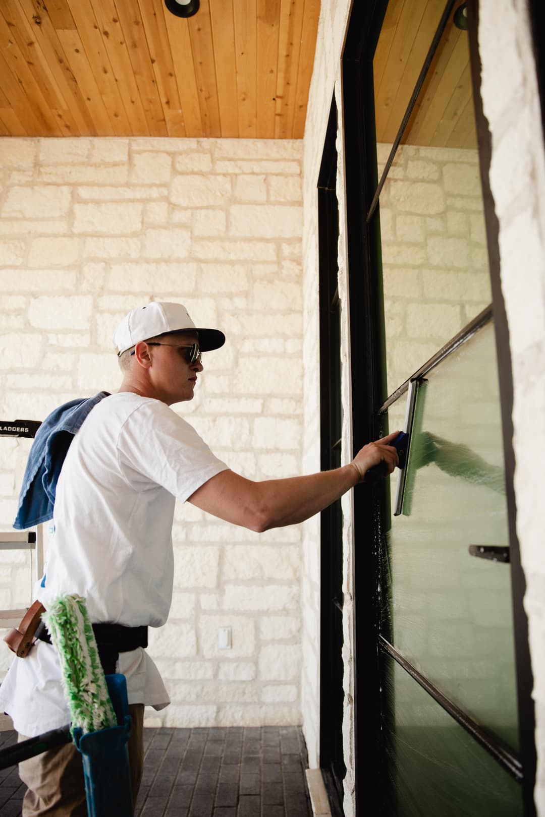 Professional window cleaner using a squeegee on a large glass door in a bright home exterior.